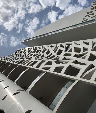 Low-angle view of a modern architectural building featuring curved balconies and a unique geometric facade, set against a partly cloudy sky